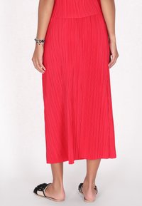 Rød plisseret maxi-skort med en glat tekstur, med et flydende design, der falder under læggen, parret med flade, afslappede sandaler.