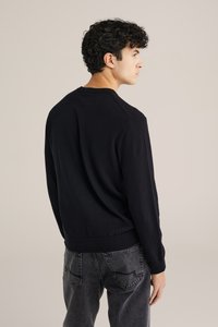 Melnā adīta virsma ar ribotu apakšmalu un piedurknēm, ar klasisku apaļu kaklu un brīvu piegriezumu. Valkātas ar tumši pelēkiem džinsiem.