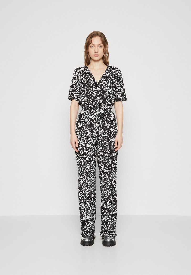 Combinaison à imprimé floral noir et blanc avec manches courtes, décolleté en V, taille cintrée et coupe droite. Tissu doux et design décontracté.