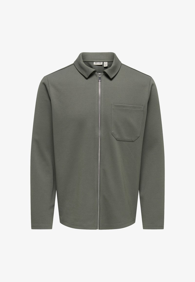 Chemise pour homme à manches longues couleur vert olive avec fermeture éclair, col et poche poitrine, en tissu texturé.