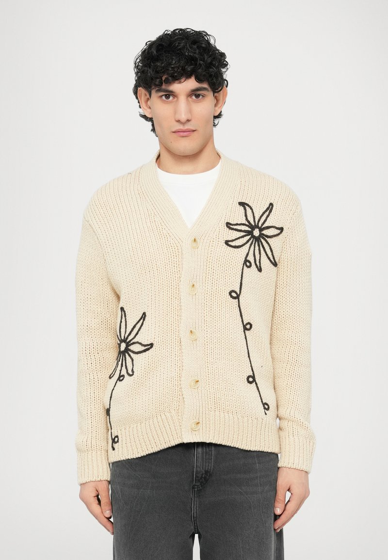 Κρεμ ζακέτα με μαύρη κεντητή λουλουδάτη διακόσμηση, διαθέτει V-λαιμόκοψη, πέντε κουμπιά, ριμπ μανσέτες και χοντρή πλεκτή υφή.