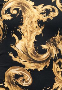 Πλούσια χρυσά στροβιλιστικά στοιχεία σε μπαρόκ στυλ με μοτίβα φύλλων σε μαύρο υφασμάτινο φόντο, με διακριτικό κείμενο σε καλλιγραφική γραφή.