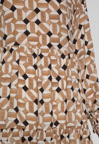 Vestido de manga larga con un patrón geométrico en marrón, blanco y negro, con detalles fruncidos en la cintura y tejido texturizado.
