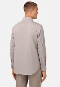 Camisa de manga larga gris claro con cuello, costuras detalladas y puños con botones. Tejido suave con un ajuste relajado y dobladillo curvado.