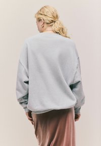 Jasnoszara, oversize bluza z opadającymi ramionami; miękka tekstura; zestawiona z długą różową satynową spódnicą; prosty, codzienny design.