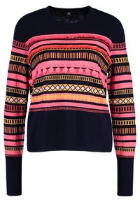 Pull marine avec des rayures géométriques roses, jaunes et noires, des pompons texturés et des détails à franges sur la poitrine et les manches.