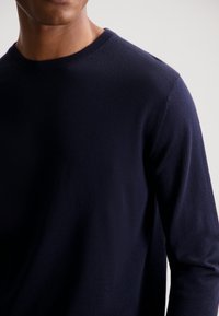 Marineblaues Strickpullover mit Rundhalsausschnitt und langen Ärmeln, der eine glatte Textur und subtile Rippdetails am Kragen aufweist.