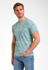 Šviesiai žalia medvilnė marškinėliai su trumpomis rankovėmis, puikuojantys lapų raštu, apvaliu kaklu ir mažu logotipo detaliu prie apvado.