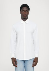 Hvit langermet skjorte med klassisk krage og knappelenk foran, laget av lett stoff, sammen med lyseblå jeans.