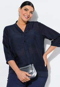 Tummansininen sifonkiblouse puolihöyhenillä, V-pääntiellä ja napilla edessä. Yhdistetty hopeametallic-laukkuun ja tummansinisiin housuihin.