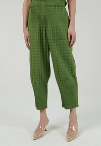 Gequilte groene broek met een gestructureerd oppervlak, voorzien van een elastische tailleband en wijde benen. Gestyled met doorzichtige hakken.