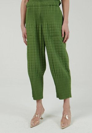 Pantalons verts matelassés avec une surface texturée, dotés d'une taille élastique et de jambes larges. Associés à des chaussures à talons transparents.