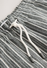 Primo piano di un tessuto a righe grigie e bianche con un cordoncino bianco annodato che passa attraverso un occhiello in metallo.