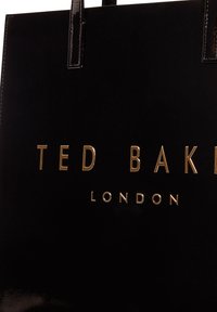 Μαύρη γυαλιστερή τσάντα tote με χρυσά γράμματα "TED BAKER" και "LONDON". Διαθέτει ίσια χερούλια και λεία, λαμπερή υφή.