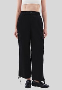 Černé širokoprsé cargo kalhoty s elastickým pasem, bočními kapsami a nastavitelnými spodními okraji. Hladký materiál s volným střihem.