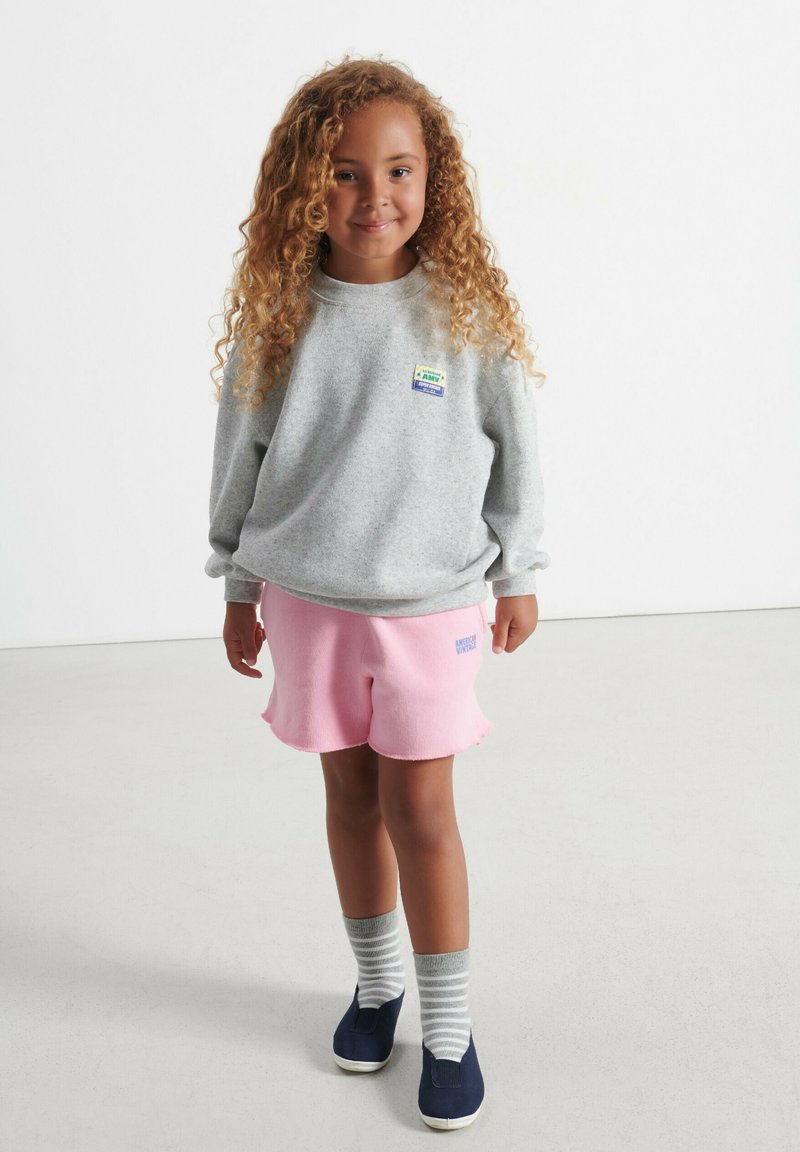 Hallitusseentehalli kapuutsiga hallid dressipluusid logoga, roosa fliisist lühikesed püksid kulunud servadega, hallid ja valged triibulised sokid ning tumesinised libisemiskindlad kingad.