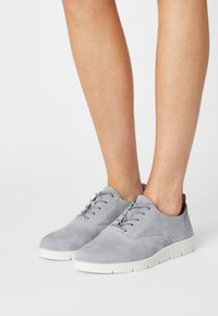 Scarpe grigie in suede con lacci, punta tonda e suola in gomma bianca. Texture liscia con cuciture tonali e design minimalista.