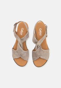 Beige suède sandalen met crossover banden, een soepele bruine voetbed en een zilveren gesps accent voor een verstelbare pasvorm, ontworpen voor comfort.