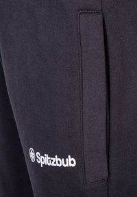 Dunkelgraue Sweatpants mit einer glatten Textur, ausgestattet mit einer Seitentasche und dem weißen "Spitzbub"-Logo auf dem Oberschenkel.