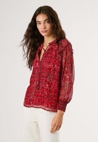 Blusa rossa con motivo paisley, colletto arricciato, maniche lunghe raccolte ai polsi e scollo regolabile con cordoncino, realizzata in tessuto leggero.