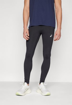 Schwarze Sportleggins aus dehnbarem Stoff, enganliegendes Design, mit einem kleinen weißen Logo. Kombiniert mit einem marineblauen Tanktop und weißen Sneakers.