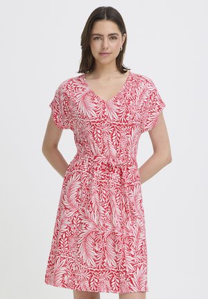 Vállig érő sötét hajú nő, aki piros-fehér virágmintás, térdig érő ruhát visel rövid ujjakkal és derékösszekötővel.