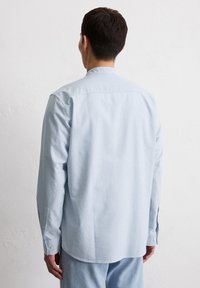 Camicia a maniche lunghe a strisce azzurre con taglio dritto e polsini con bottoni, realizzata in un tessuto morbido. Presenta un colletto e un design semplice.