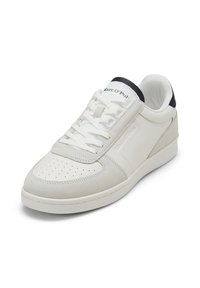Baskets basses blanches avec embout perforé, laçage à l’avant, empiècements en daim et cuir, et languette de talon noire, inclinées vers la gauche sur fond blanc.