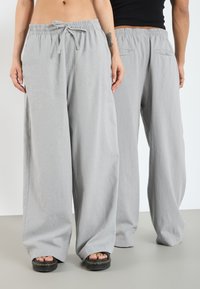 Pantalons larges gris clair avec une taille élastique et un cordon de serrage. Comprend deux poches arrière et un tissu doux et texturé.
