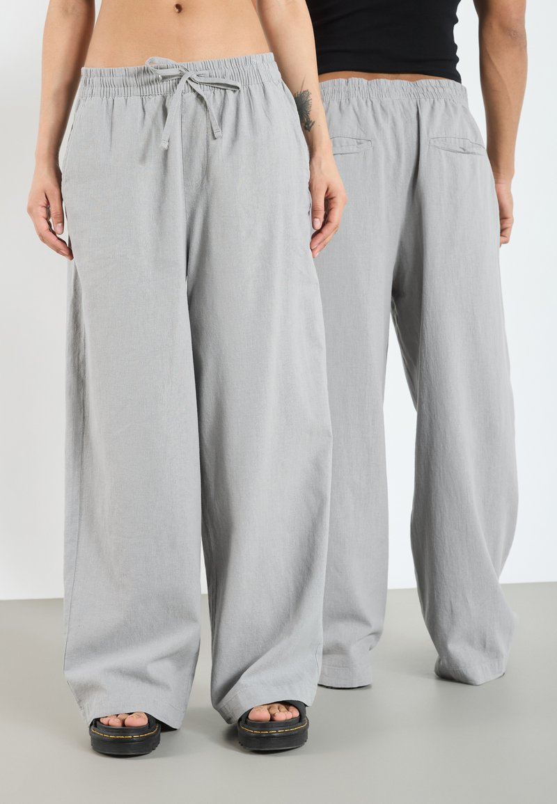Pantalons larges gris clair avec une taille élastique et un cordon de serrage. Comprend deux poches arrière et un tissu doux et texturé.