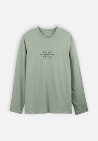 T-shirt en coton vert à manches longues avec un col rond. Présente un graphisme central avec le mot "OXBOW" et des motifs symétriques dans des couleurs sombres.