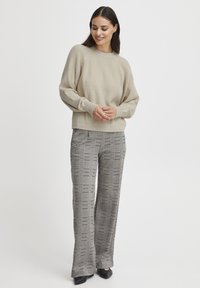 Pull en tricot texturé beige avec des manches raglan associé à un pantalon à carreaux noir et blanc taille haute, complété par des chaussures noires.