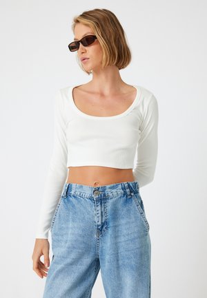 Witte, geribbelde, lange mouw crop top met een brede ronde hals, gecombineerd met hoge taille, lichtblauwe denim jeans.