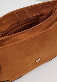 Hnědá semišová taška s několika vnitřními kapsami, měkkou texturou a jednoduchým cvokem. Má hladkou vnitřní podšívku.