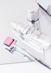 Kollagenterapi gel i en klar flaske med sølvdetaljer, parret med en microneedling roller med et pink hoved, hvilende på en reflekterende overflade.