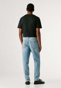 Černé crop tričko, světle modré džínové kalhoty a černé šněrovací boty. Rovný střih džín s zadními kapsami a viditelnými švy.