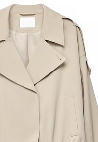 Trench-coat beige avec larges revers, épaulette à l'épaule, une poche poitrine et une texture de tissu lisse.