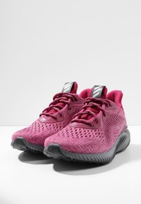 Baskets de sport roses en mesh avec une finition texturée, dotées d'une semelle en caoutchouc grise et d'accents noirs sur la languette et les lacets.