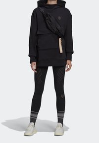 Czarna, oversize bluza z kapturem, torba na ramię, teksturowane czarne legginsy w kropki oraz białe sneakersy. Minimalistyczny design, luźny krój.