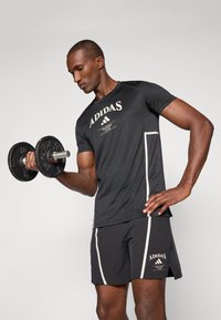 Black short-sleeve athletic shirt with white "ADIDAS" logo and training club text, paired with matching black shorts featuring white accents.