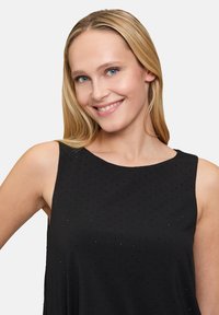 Schwarzes ärmelloses Oberteil mit rundem Ausschnitt, gefertigt aus einem strukturierten Stoff, der mit kleinen, subtilen Punkten verziert ist, um zusätzliche Details zu bieten.