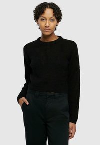 Maglione corto nero a maglia con texture a coste, scollo rotondo e maniche lunghe, abbinato a pantaloni scuri.