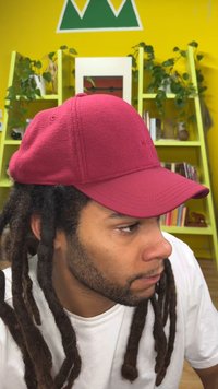 Casquette bordeaux en tissu texturé, dotée d'une visière incurvée et de détails de coutures discrètes. L'arrière possède une fermeture à bouton unique.