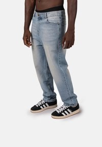 Jasnoniebieskie dżinsy z wyblakłym wykończeniem, w fasonie prostych nóg, z przednimi kieszeniami i małym haftowanym logo, zestawione z czarnymi trampkami.