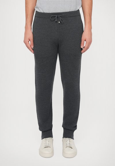 Joggers gris charbon en tissu doux et texturé, dotés d'une taille élastique, d'un cordon de serrage et de poignets côtelés. Portés avec des baskets de couleur claire.