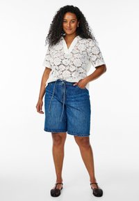 Blouse en dentelle blanche à manches courtes et décolleté en V, associée à un short en jean bleu avec une taille à cordon et des poches.