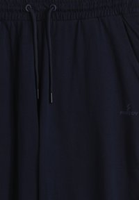 Pantalones deportivos azul marino hechos de tela suave, con cintura elástica y cordón ajustable, y bolsillos laterales. Branding sutil en la parte inferior lateral.