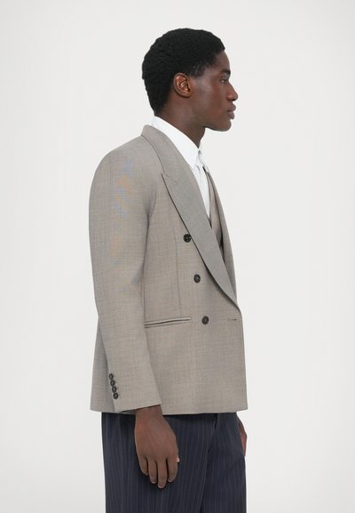 Grau doppelbrüstiger Blazer aus strukturiertem Stoff, mit spitzen Revers, schwarzen Knöpfen und zwei Seitentaschen. Kombiniert mit einem weißen Hemd darunter.