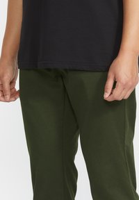 Zwarte katoenen T-shirt gecombineerd met donkergroene broeken. Het T-shirt heeft een ronde halslijn en een rechte zoom; de broek is taps toelopend met een gladde textuur.