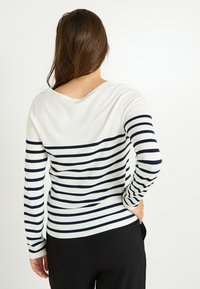 Suéter de punto a rayas con rayas horizontales en azul marino y blanco, un escote ancho y mangas largas, combinado con pantalones negros.